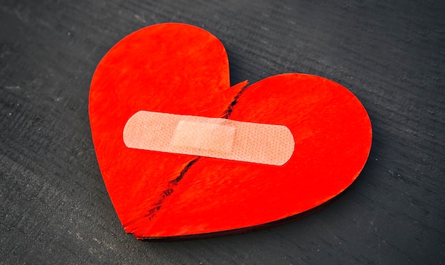 Dwie części czerwonego złamanego drewnianego serca przyklejone plastrem Koncepcja przebaczenia odnowienia relacji i uzdrowienia