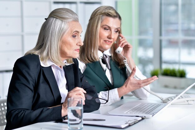 Zdjęcie dwie dojrzałe biznesmenki siedzące przy stole z laptopem i pracujące razem