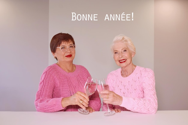 Zdjęcie dwie dojrzałe kobiety w różowych sweterkach piją wino i świętują.