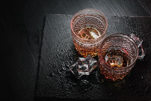 Zdjęcie dwie drogie szklanki whisky z lodem na czarnej kamiennej tacy