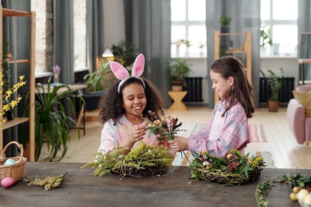 Dwie dziewczynki siedzące przy stole i robiące wieniec z kwiatów na Święta Wielkanocne