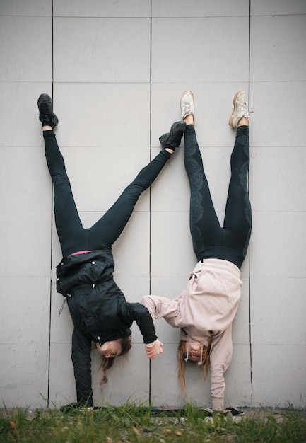 Dwie dziewczyny akrobatki trzymające się za ręce wykonujące stanie na rękach na tle ściany