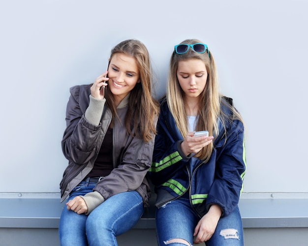 dwie dziewczyny chodzące po ulicach śmiejąc się robiąc zdjęcia za pomocą smartfona