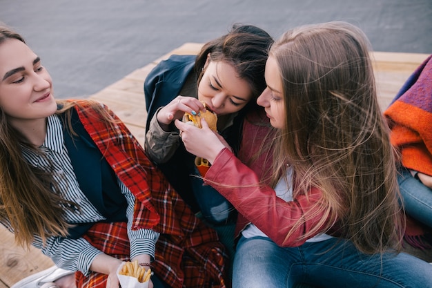 Zdjęcie dwie dziewczyny dzielące się jednym burgerem. bliska przyjaźń. niezwykłe miejsca wypoczynku i komunikacji, wspólne spędzanie czasu, koncepcja wesołej i radosnej atmosfery