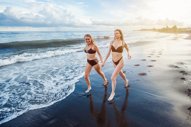 Dwie dziewczyny dziewczyny w czarnych strojach kąpielowych uprawiają sport na plaży