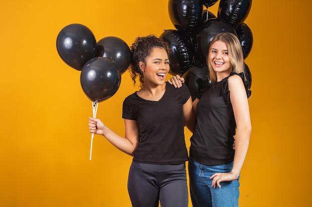 Dwie dziewczyny na żółtym tle z czarnymi balonami na imprezie promocyjnej w czarny piątek.