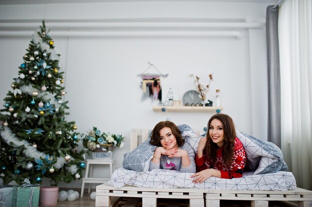 Dwie dziewczyny noszą zimowe swetry bawiące się na łóżku w pokoju z dekoracjami chrismas.