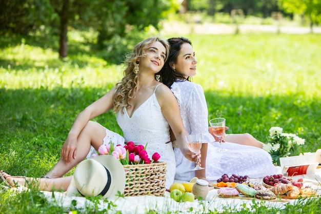 Dwie dziewczyny odpoczywają w parku na kocu piknikowym z owocami i winem