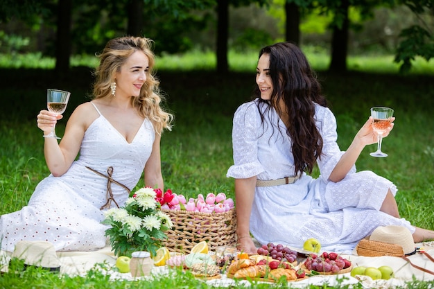 Dwie dziewczyny odpoczywają w parku na kocu piknikowym z owocami i winem