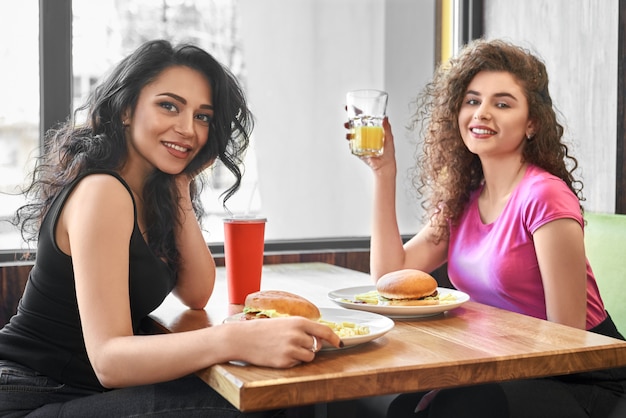 Dwie dziewczyny siedzą w kawiarni w pobliżu okna, jedząc fast food.