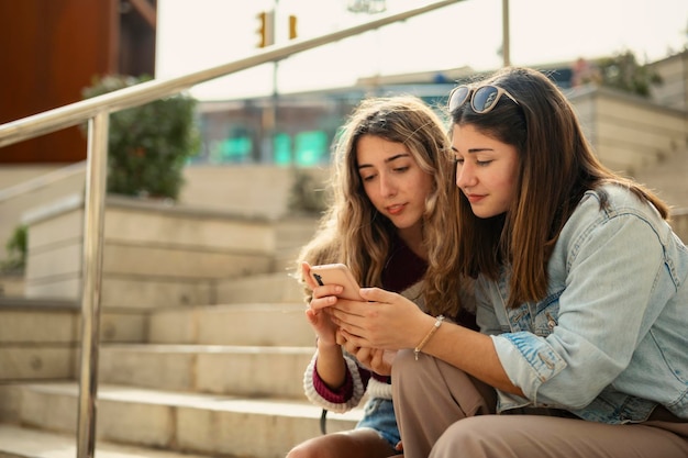 Zdjęcie dwie dziewczyny siedzące na schodach patrzące na telefon komórkowy