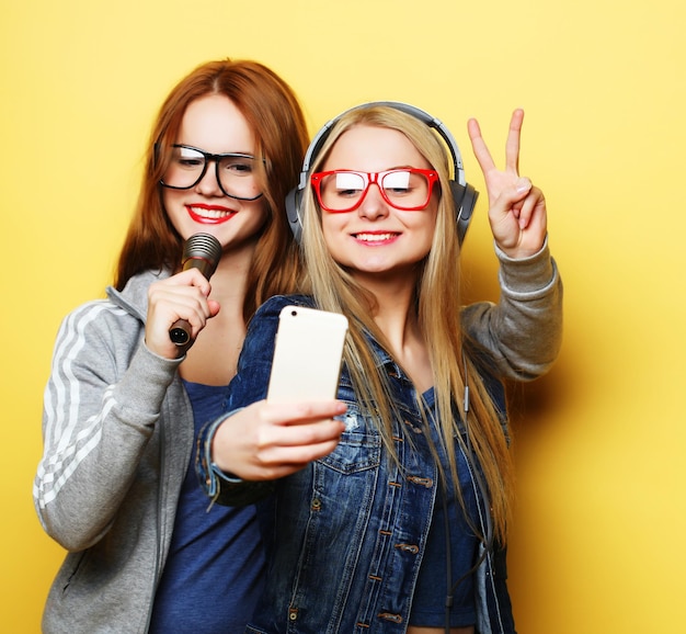 Dwie dziewczyny śpiewające i bawiące się razem z mikrofonem robią selfie