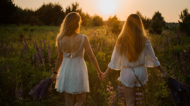 Dwie dziewczyny stojące na polu z bukietami fioletowych kwiatów