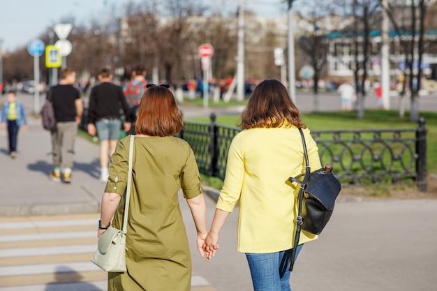 Dwie dziewczyny trzymają się za ręce i idą Ludzie przechodzą przez przejście dla pieszych na ulicy miasta