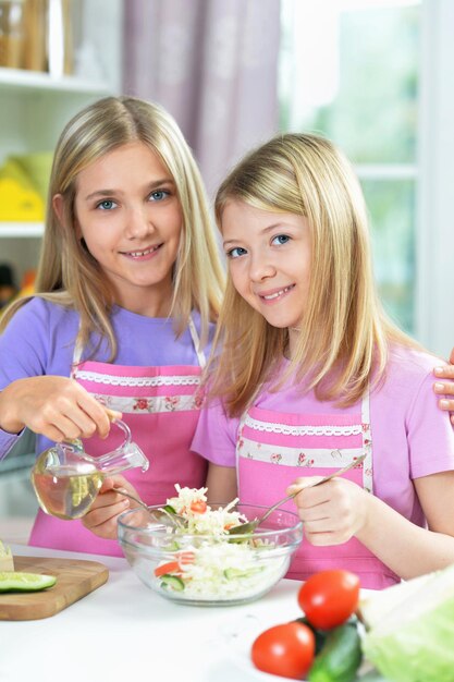 Zdjęcie dwie dziewczyny w różowych fartuchach przygotowujące sałatkę na stole w kuchni