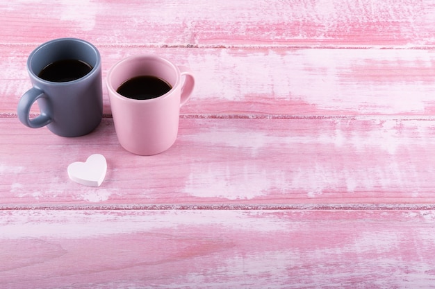 Dwie filiżanki kawy i białe serce na różowym drewnianym