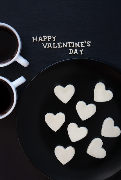 Dwie filiżanki kawy i czekoladowe cukierki z białym sercem - napis Happy Valentine