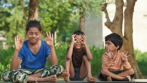 Zdjęcie dwie indyjskie dziewczynki i chłopiec medytują jogę na matce z zamkniętymi oczami w parku.