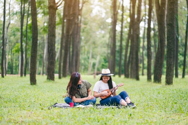 Dwie kobiety grające na ukulele, siedząc razem w lesie