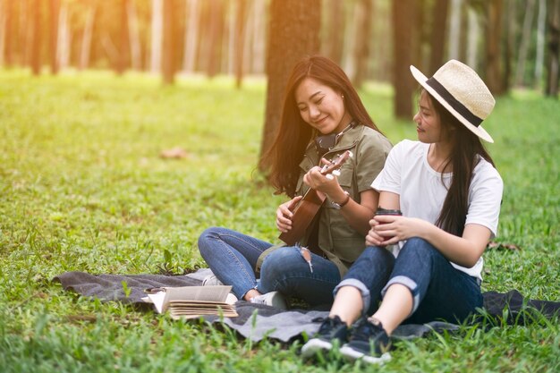 Dwie kobiety grające na ukulele, siedząc razem w lesie