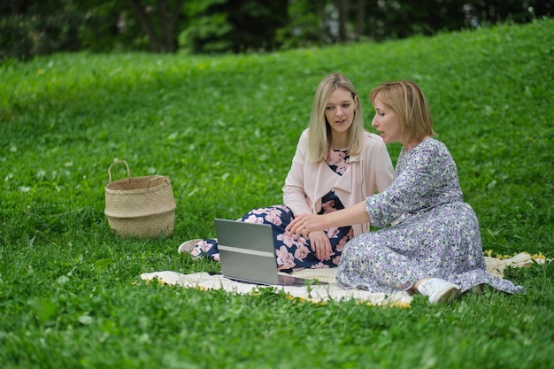 Dwie kobiety siedzą na kocu, jedna z nich pisze na laptopie.