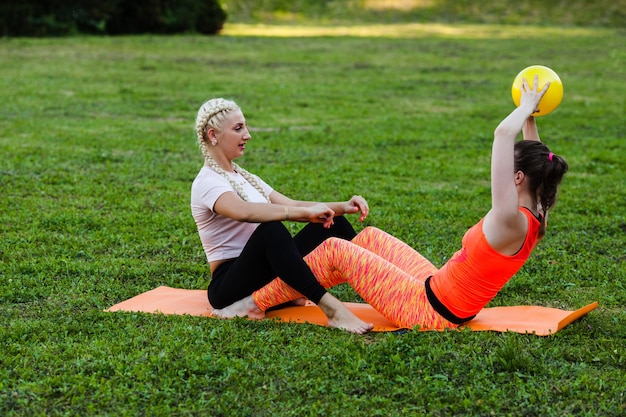 Zdjęcie dwie kobiety siedzą na macie fitness w parku i wykonują ćwiczenie z piłką