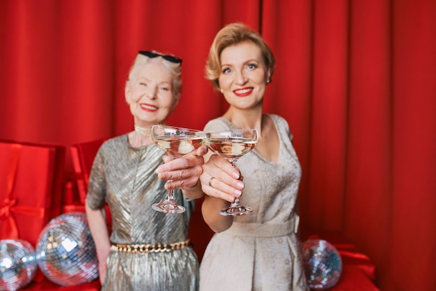 dwie kobiety starsze i starsze obchodzi Nowy Rok, trzymając w rękach szklanki białego wina musującego.