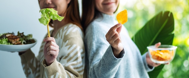 Zdjęcie dwie kobiety trzymające i pokazujące sałatkę warzywną i chipsy ziemniaczane dla koncepcji opieki zdrowotnej