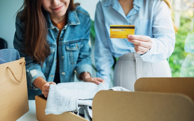 Dwie kobiety trzymające i używające karty kredytowej do robienia zakupów online podczas otwierania skrzynki pocztowej z odzieżą w domu