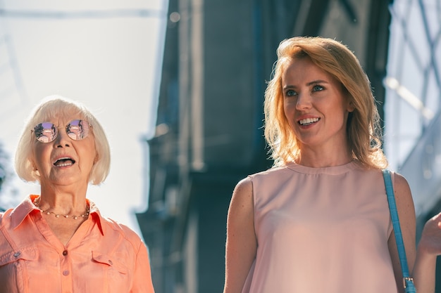 Dwie kobiety w różnym wieku stojące na zewnątrz w słoneczną pogodę i wyglądające na zaskoczone
