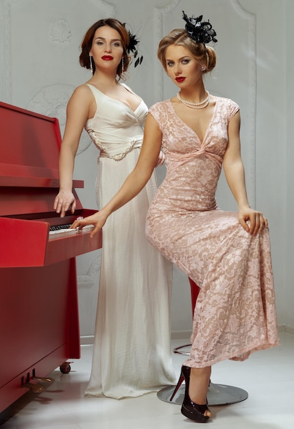 Zdjęcie dwie kobiety w ubraniach retro i kapeluszach w pobliżu fortepianu.