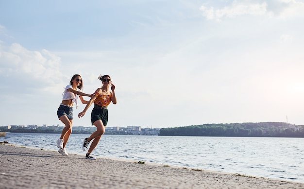 Dwie koleżanki biegają i bawią się na plaży nad jeziorem w słoneczny dzień.