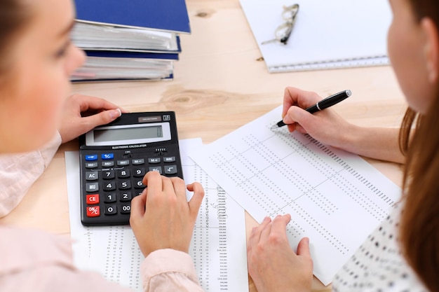 Zdjęcie dwie księgowe kobiece liczenie na dochód kalkulatora do wypełnienia formularza podatkowego ręce zbliżenie. inspektor urzędu skarbowego sprawdzający dokument finansowy. planowanie budżetu, koncepcja audytu