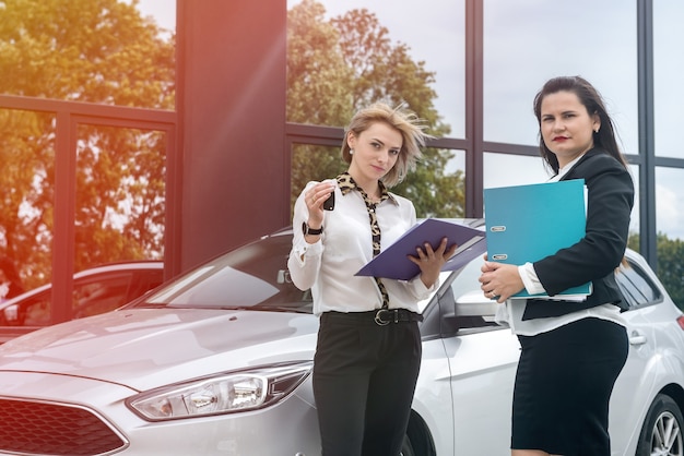 Dwie ładne kobiety z folderami stojący w pobliżu nowego samochodu. Sprawdzają niektóre dokumenty w folderach