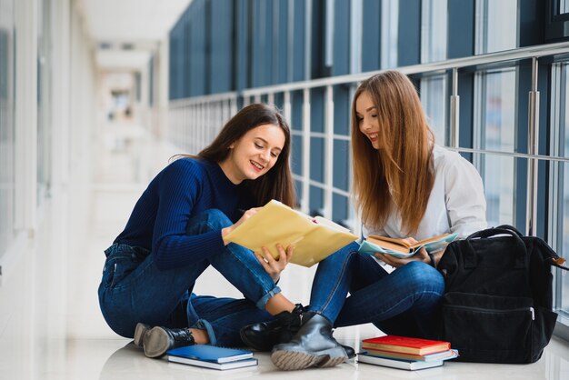 Dwie ładne Studentki Z Książkami Siedzą Na Podłodze W Korytarzu Uniwersytetu