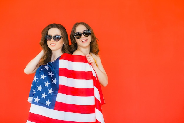 Dwie ładne, stylowe dziewczyny świętujące Dzień Niepodległości i bawiące się nad narodową flagą USA na czerwono