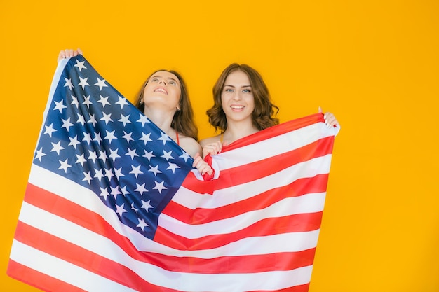 Dwie ładne, stylowe dziewczyny świętujące Dzień Niepodległości i bawiące się nad narodową flagą USA