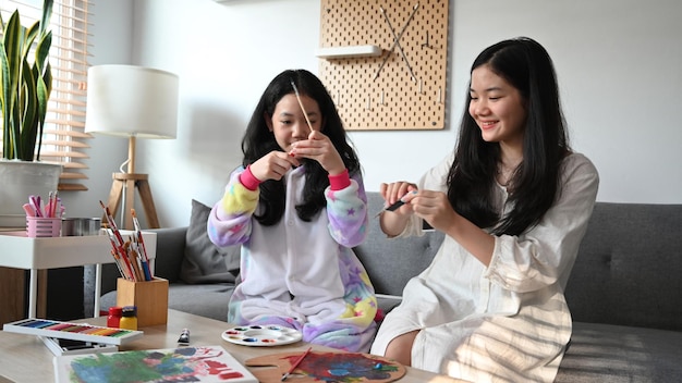 Dwie małe Azjatki malują razem akwarelą w domu w weekend
