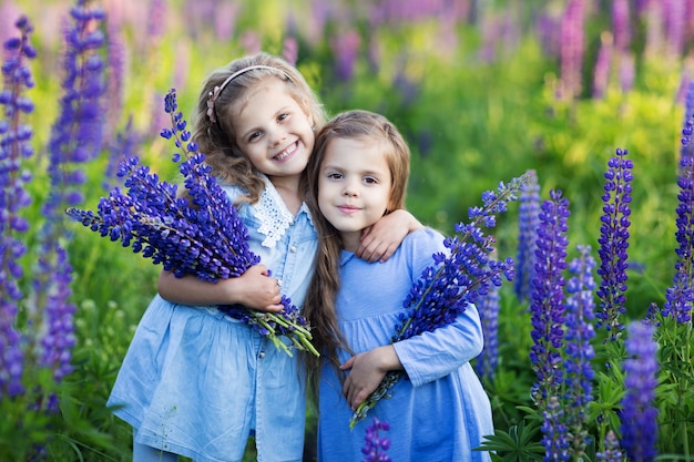 Dwie Małe Dziewczynki Przytulają Się I Uśmiechają, Trzymając W Rękach Kwiaty W Polu Fioletowych Kwiatów