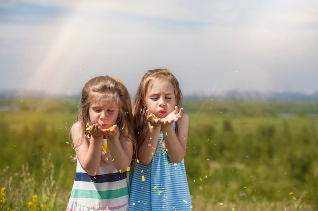 Zdjęcie dwie małe dziewczynki są pięknymi dziećmi w naturze, dmuchającymi konfetti w słońcu