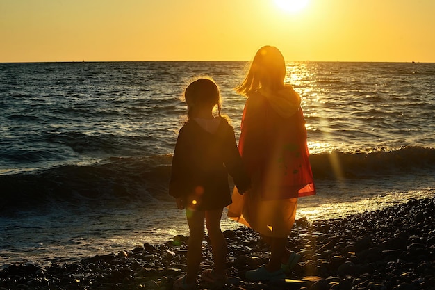 Dwie małe dziewczynki wieczorem na plaży patrzą na piękny zachód słońca nad morzem