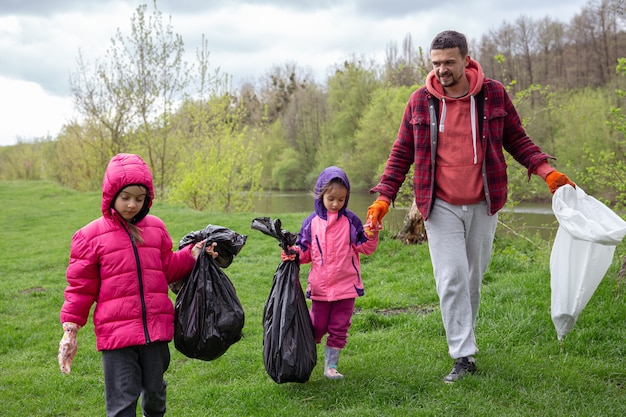 Dwie Małe Dziewczynki Z Tatą, Z Workami Na śmieci Na Wycieczce Do Natury, Sprzątają środowisko.