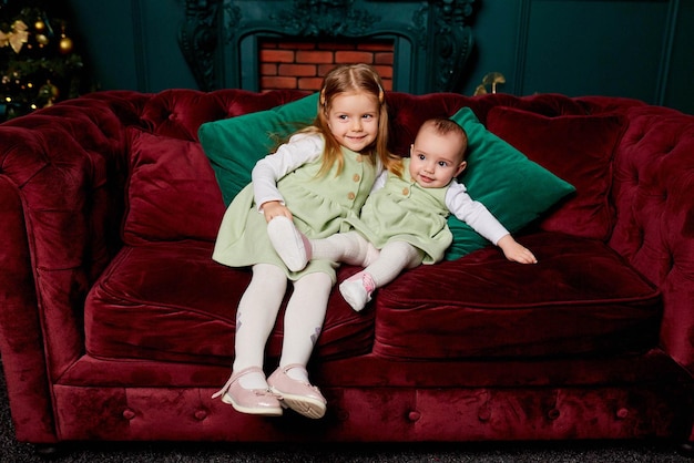 Dwie małe siostry siedzą na czerwonej kanapie