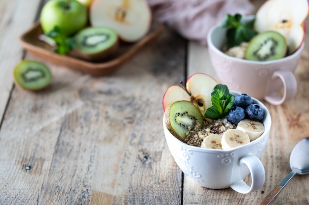 Dwie miski płatków owsianych lub muesli z jagodami, jabłkiem, miodem i miętą na rustykalne drewniane tła. Skopiuj miejsce