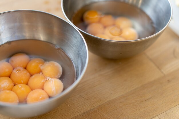 Dwie misy ze stali nierdzewnej wypełnione wieloma pękniętymi jajkami z całymi żółtkami, w drewnianym stole. Ścieśniać.