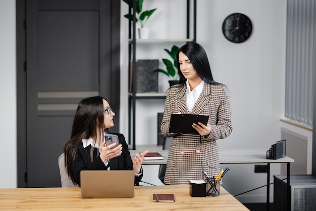 Dwie młode atrakcyjne kobiety pracują w biurze Kobieta rozmawia przez telefon, a jej kolega robi notatki w zeszycie