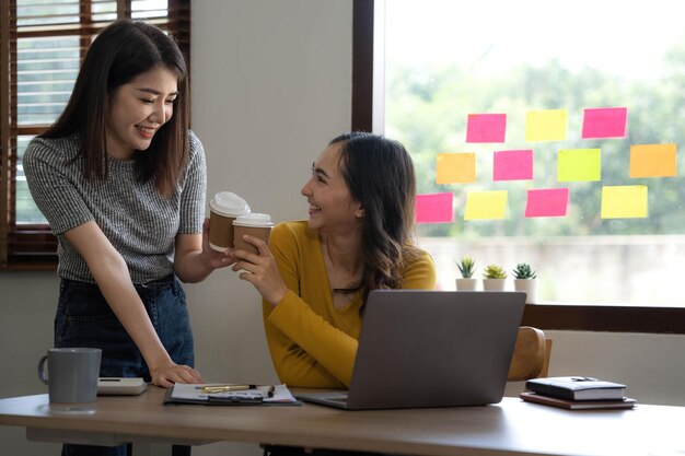 Dwie młode azjatyckie kobiety biznesu rozmawiają konsultują omówienie pracy z prezentacją nowego pomysłu na projekt startowy analizują plan marketingowy i inwestycje w biurze