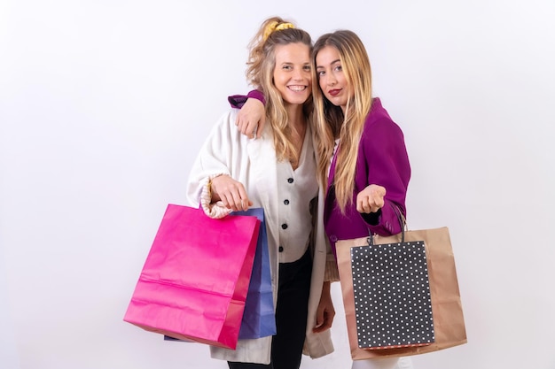 Dwie młode blond kobiety rasy kaukaskiej, przyjaciółki, robią zakupy w sprzedaży, przytulając się do papierowych toreb