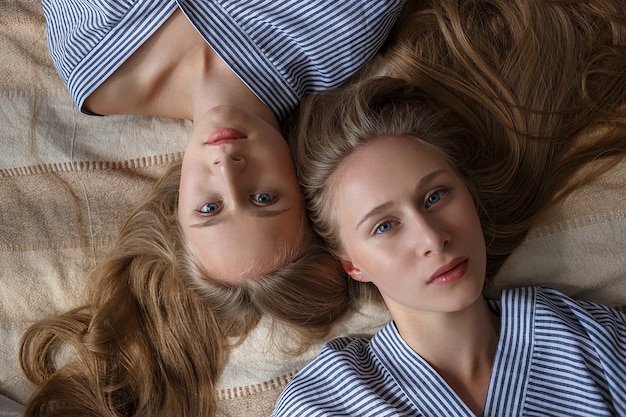 Dwie młode całkiem kaukaskie bliźniaczki w pasiastych oversize koszulach leżących na kanapie