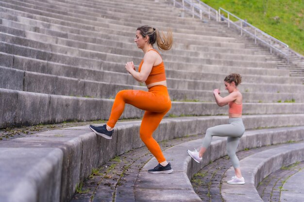 Dwie młode dziewczyny fitness w parku miejskim ćwiczą nogi na schodach